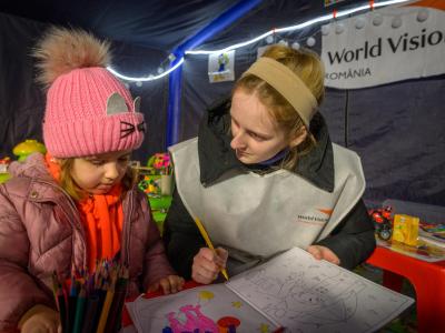 Nicolete Turcu, helps 4-year-old Arina with her coloring inside World Vision World Vision's child play area in Husi, Romania.