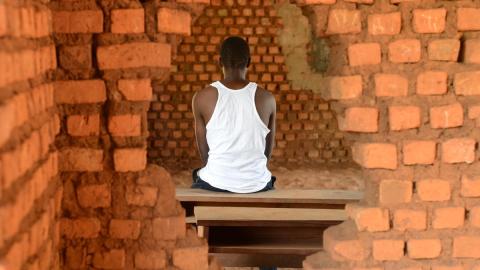 A former child soldier from South Sudan sits framed by a whole in the wall