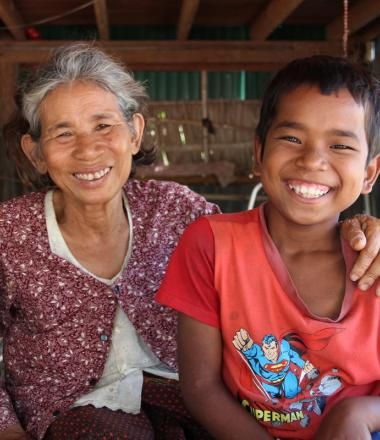 12 year old Khmer boy sits with his grandmother, they are both smiling at the camera.