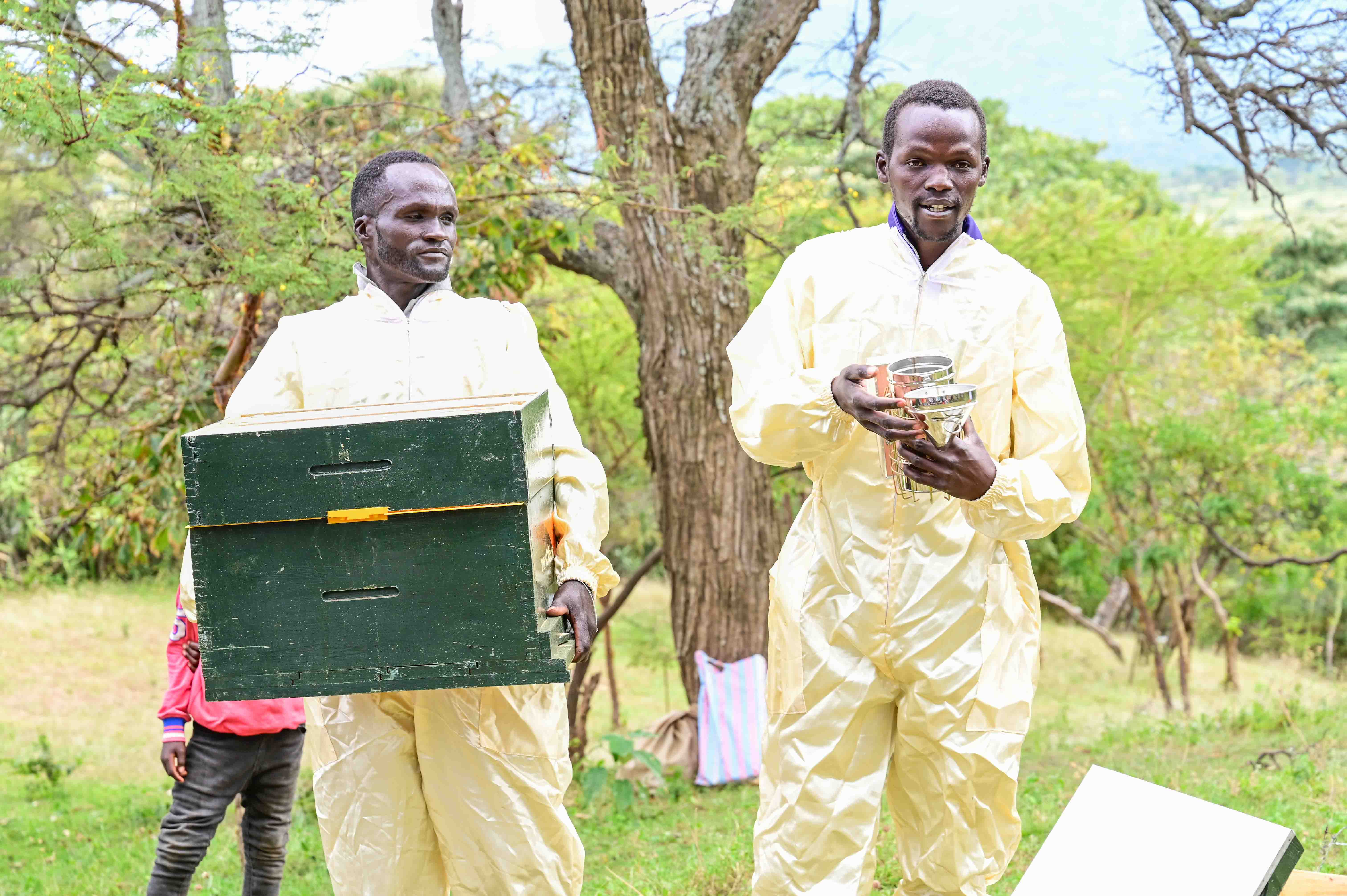 Samwel Musto (left) holding a Langstroth hive and Richard Mnang’at (right) holding a smoker during a community meeting with farmers in West Pokot County. ©World Vision Photo/ Hellen Owuor