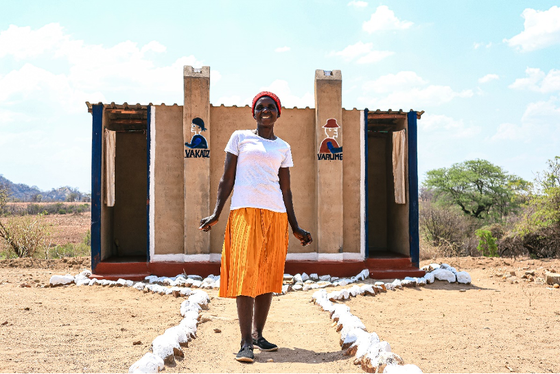 Chipo proudly standing in front of her latrine toilet