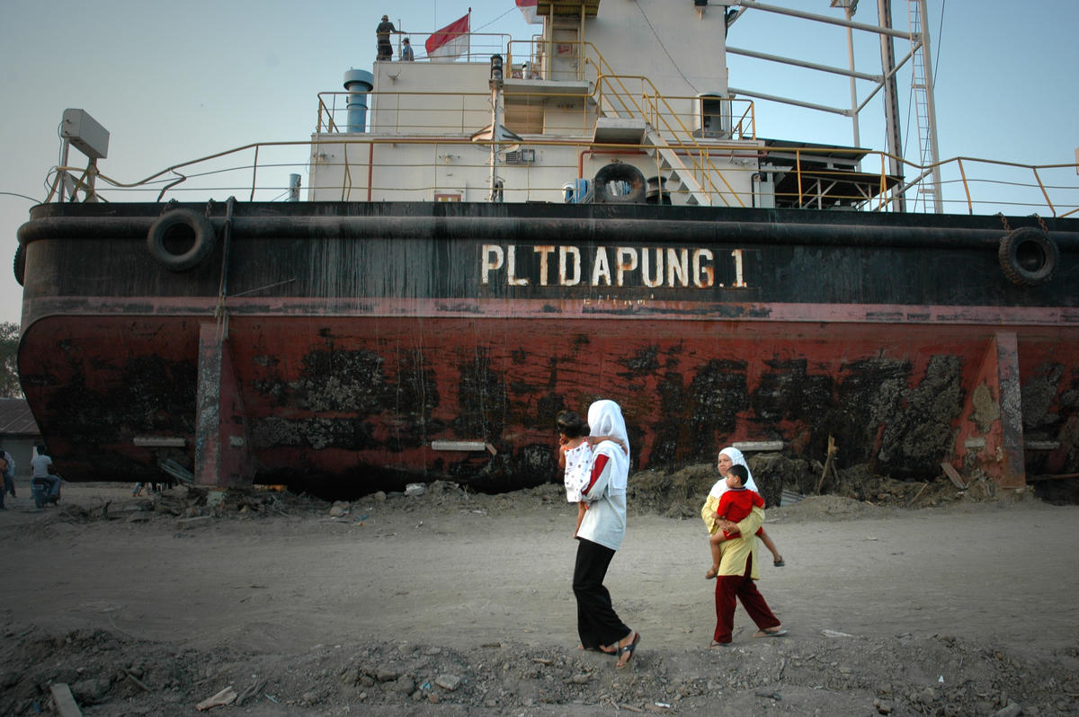 People in Aceh walk past a floating power boat