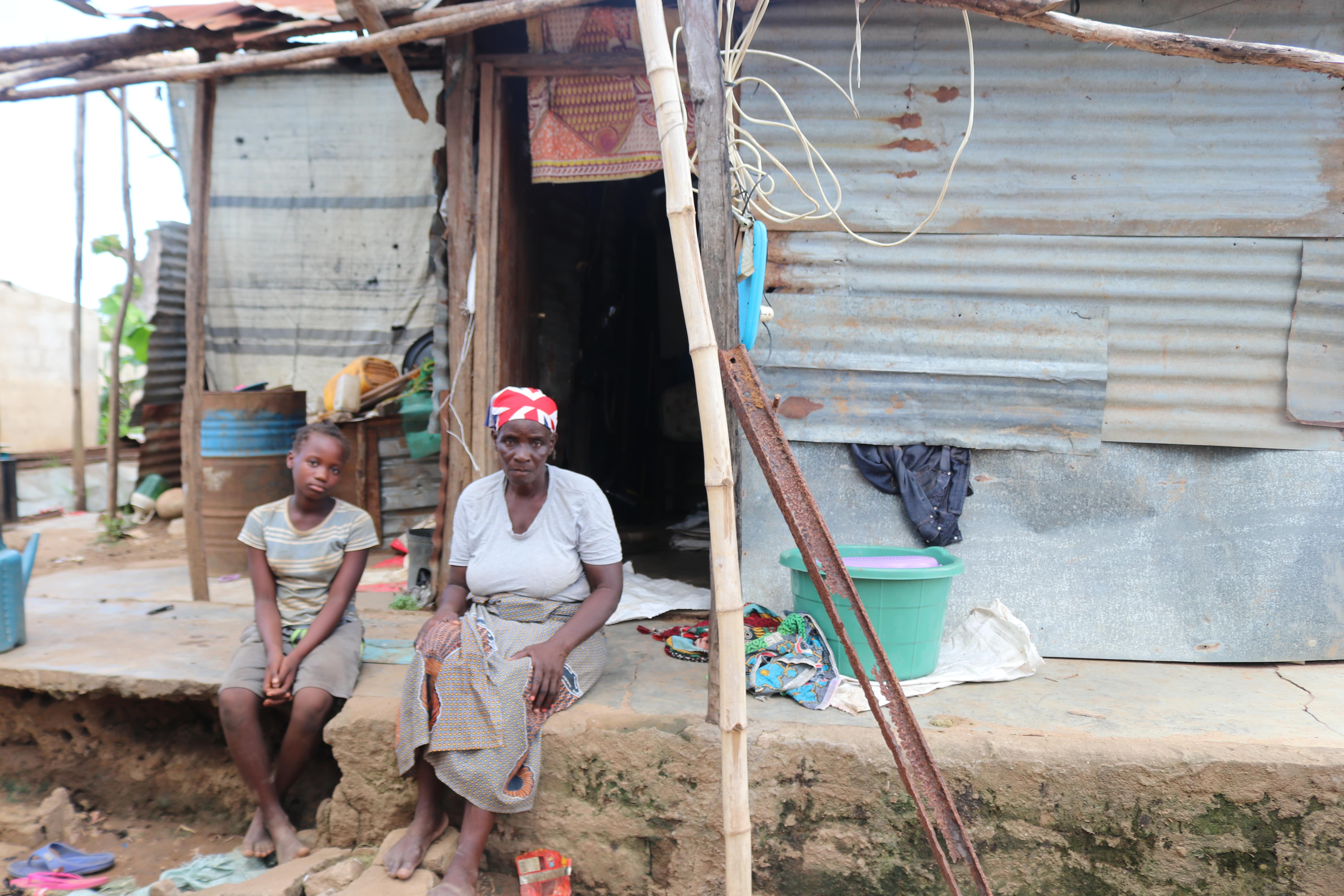 Amélia and her grand daugther are sitting in front of their wood-and-zinc house after rebuilg