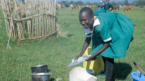 Mitchell helps her mother in washing the dishes as she watches her friends continue playing in the playground near her home. ©World Vision Photo/Peter Mwaura