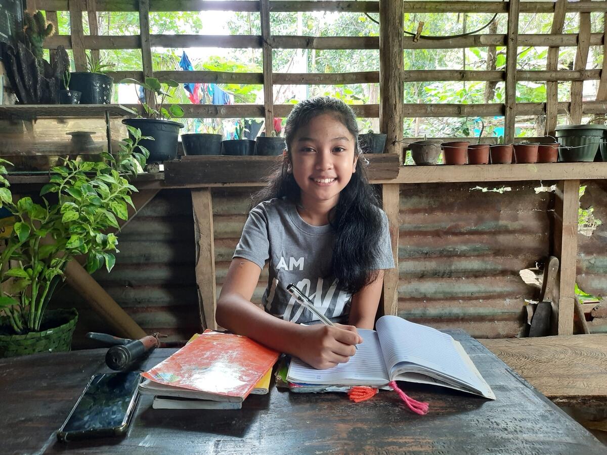 Nexi sits with her books on her desk to learn in the Philippines