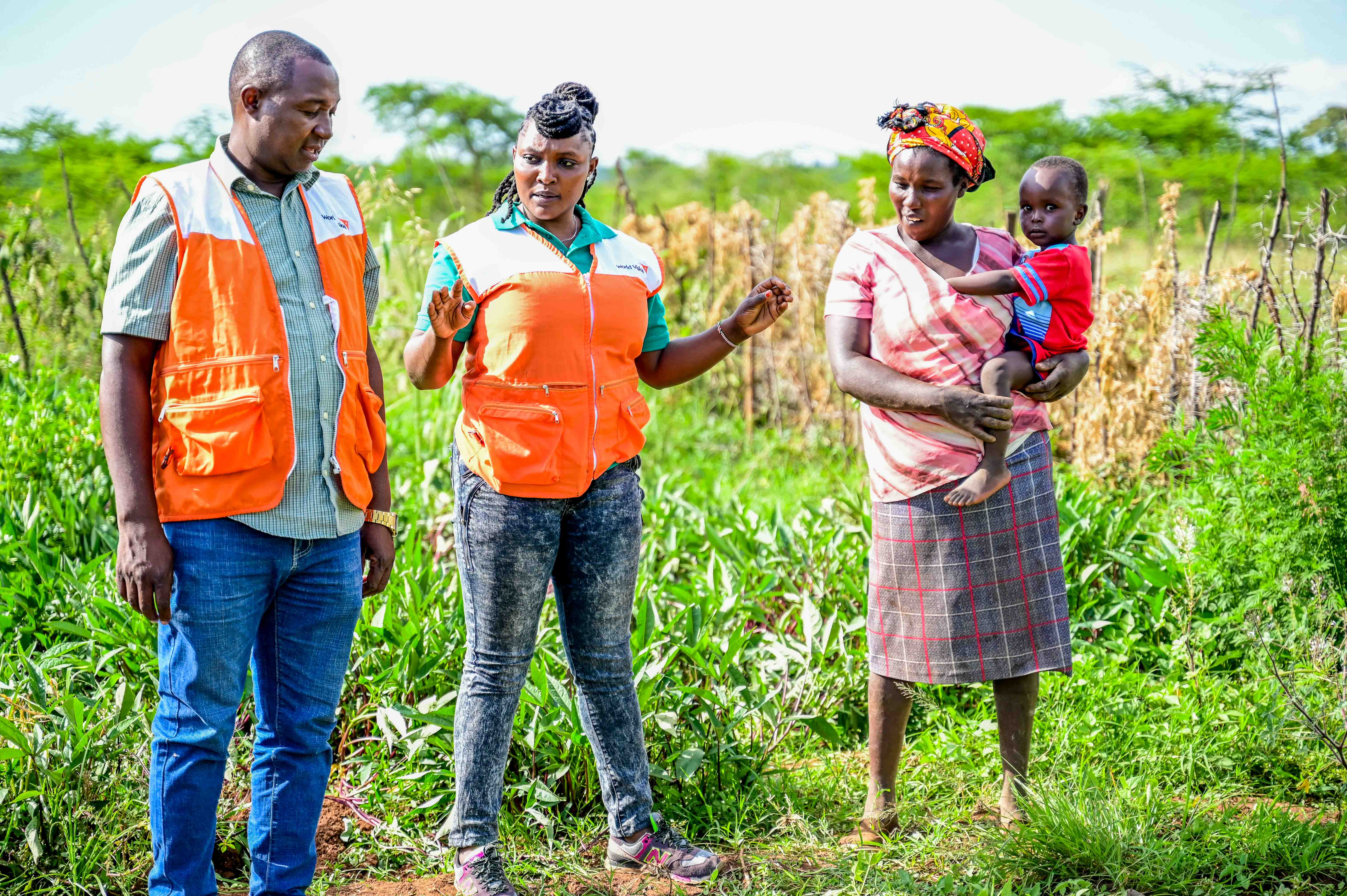 World Vision Kenya staff (Henry and Mary) at Sally’s farm. “Frequent visits from World Vision keep me on my toes, so I ensure that my farm is always good condition as we were trained,” Sally says . © World Vision Photo/Hellen Owuor.