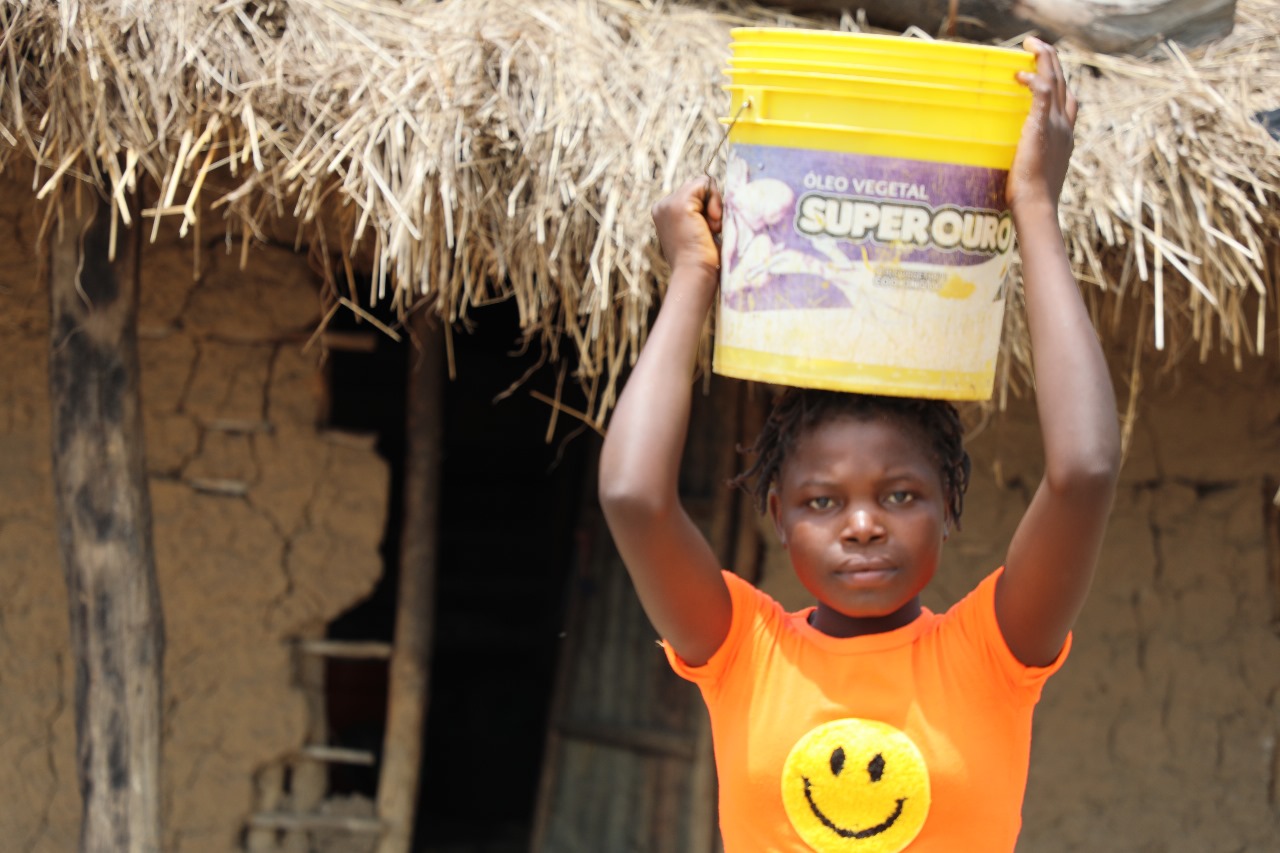 Claudina with a bucket of water in her head in her daily journey to fetch water,