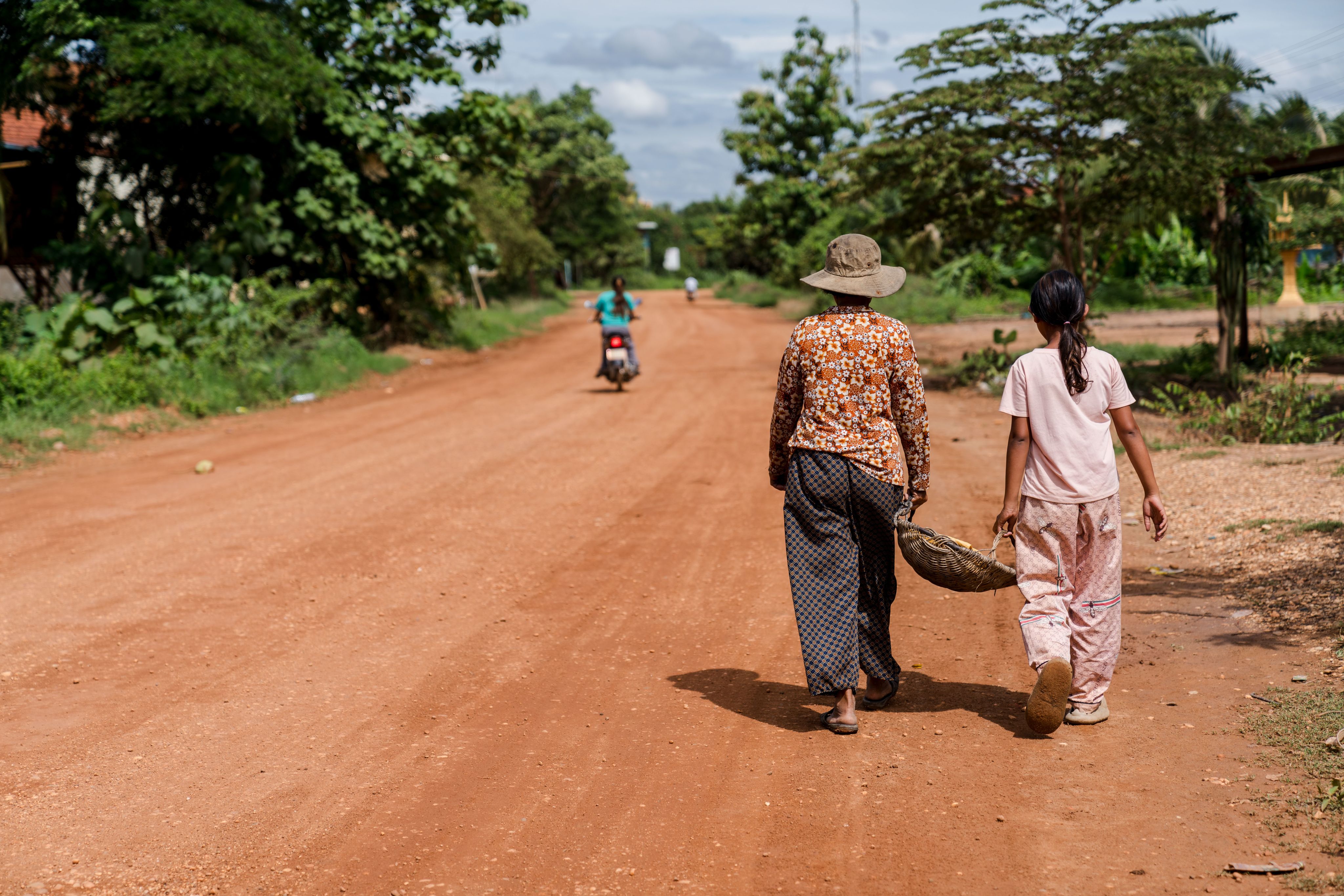 Migrant child and caretaker carrying a basket together down a dirt road