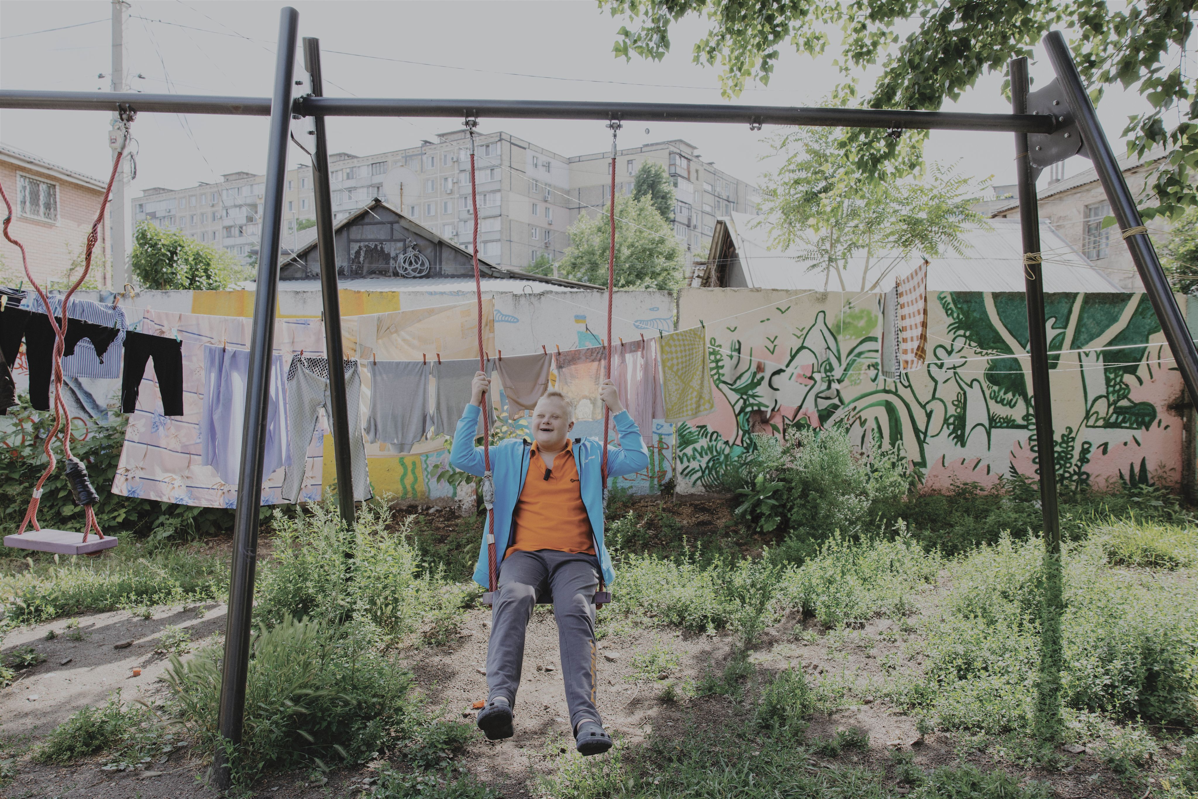 Young boy with special needs sits on a swing outside the shelter where they are currently living in Ukraine