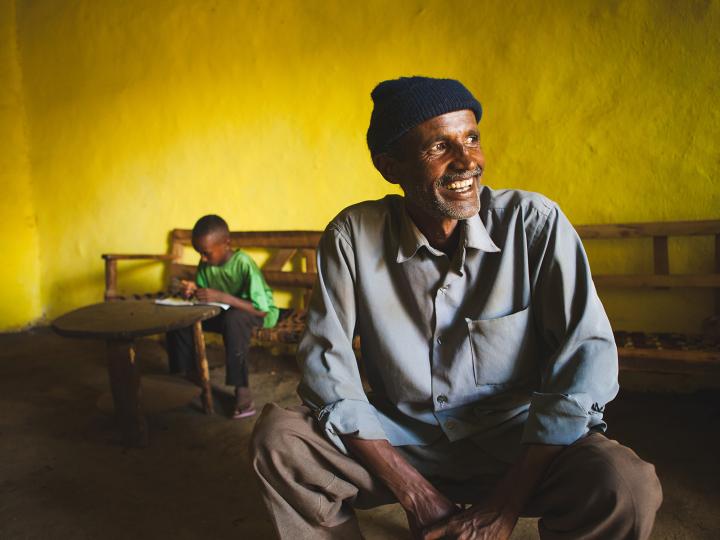 An Ethiopian man in his home with his son reading in the background
