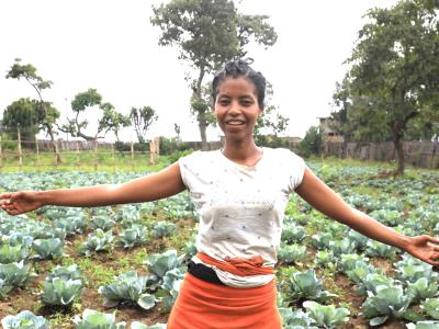 Tseganesh smiling at her parent's garden full of vegetables