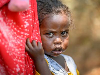 A little girl peers out from behind her mother's dress.