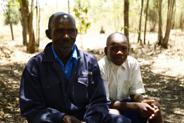 Charles with his son Biron resting in the shade of trees in the farm on a hot day.