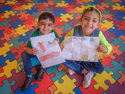 Seven-year-old Aya and her 5-year-old brother, Hamza, hold up pictures that they drew at World Vision's early childhood education and psychosocial support program.