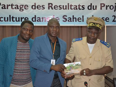 World Vision's ZonalOperations Manager for South and Western Mali region, Adama Keita (centre), hands over the final Eco Agricultural report to the chief of Diema Prefecture, Abou Diarra (right).