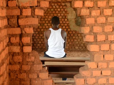 A former child soldier from South Sudan sits framed by a whole in the wall