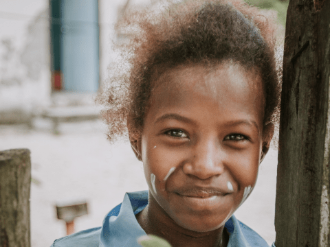 young child stands outside next to a tree