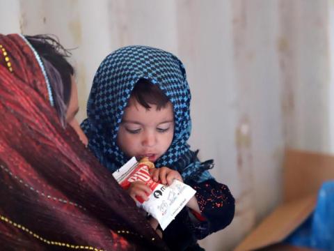 child is held by his mother and is eating a nutritional supplement 