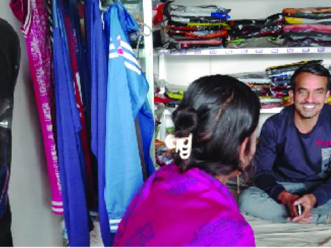 A man and a woman sitting in a clothing store. The man is smiling. 