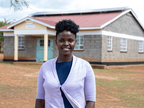 Dominica Chelatan stands outside the school where she found refuge from FGM