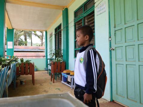 10-year-old Jubani, stands outside the entrance to his school