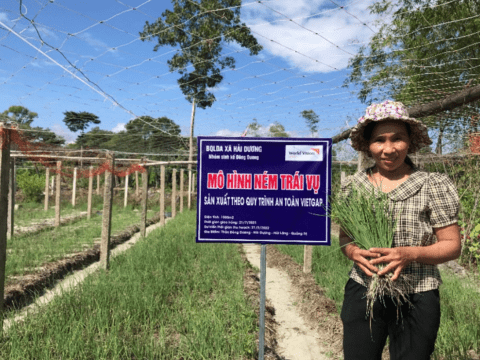 Vietnamese member of the Building Secure Livelihoods project stands infront of crops 