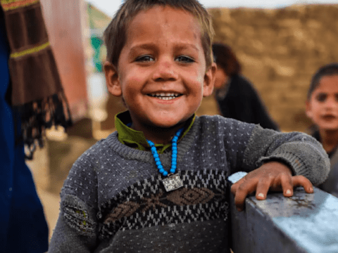 Boy smiling at camera wearing a blue necklace