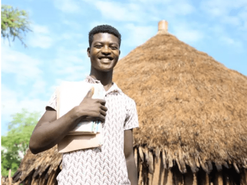 man giving thumbs up in front of hut