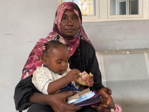 Rughia with her one year old daughter at a cash distribution centre 