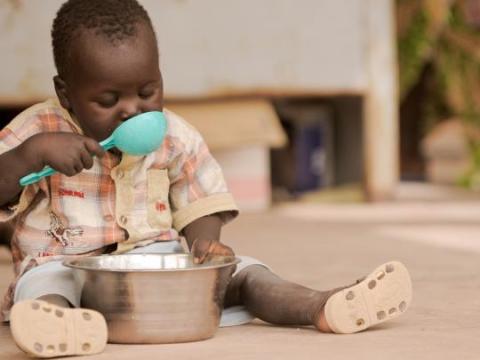 Child in mali eating with a bright turquoise spoon