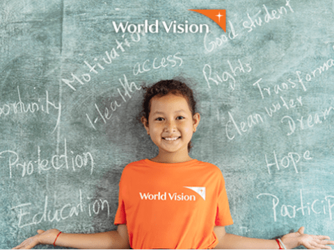 A girl in a World Vision orange T-shirt standing before a blackboard 