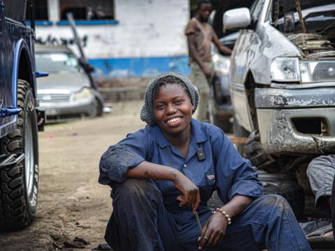 Immaculée, 18, poses next to damage cars she intends on fixing at the Sotraki garage