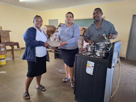 World Vision’s Development Facilitator for Gege Area Program, Nelisiwe Mhlanga, hands over cooking practical lesson supplies to Headteacher Jeremiah Dludlu and teacher Tiny Dlamini.