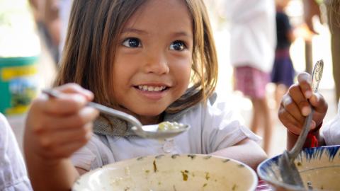 Khmer girl ginning as she holds spoon with nutritious porridge, Cambodia.