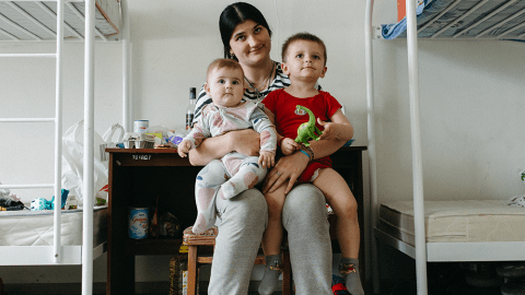 Displaced mother sits with her young children in a shelter where she receives support from World Vision