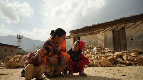 A mother and her children smile in front of a damaged house in Jajarkot