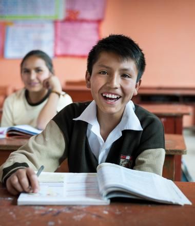 Image shows boy with textbook in school classroom