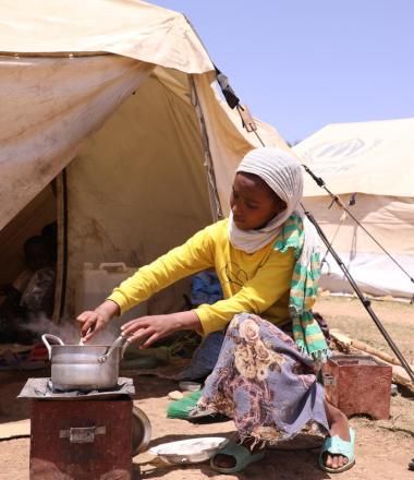 girl sits outside tent mixing food in a pot