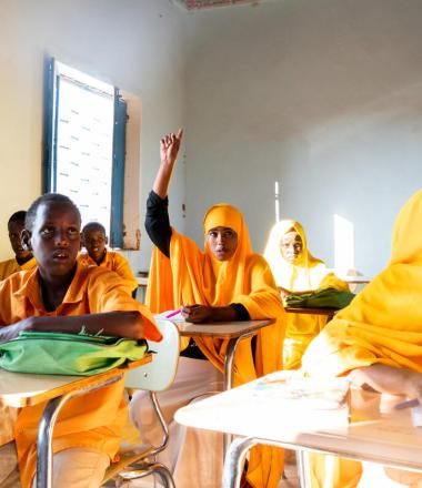 young girl in classroom full of students raises her hand