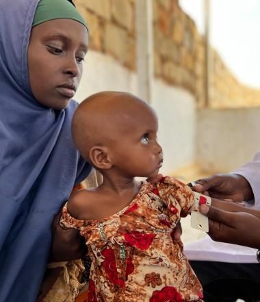 Mother holding her child as his mid upper arm circumference is tested for malnutrition