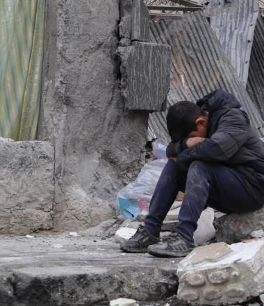 A child sitting amidst a collapsed neighbourhood in Aleppo